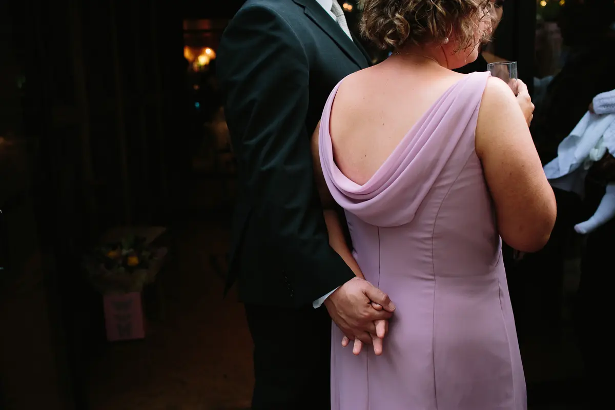 Guest in a lilac dress holding hands behind her back with a man in a dark suit