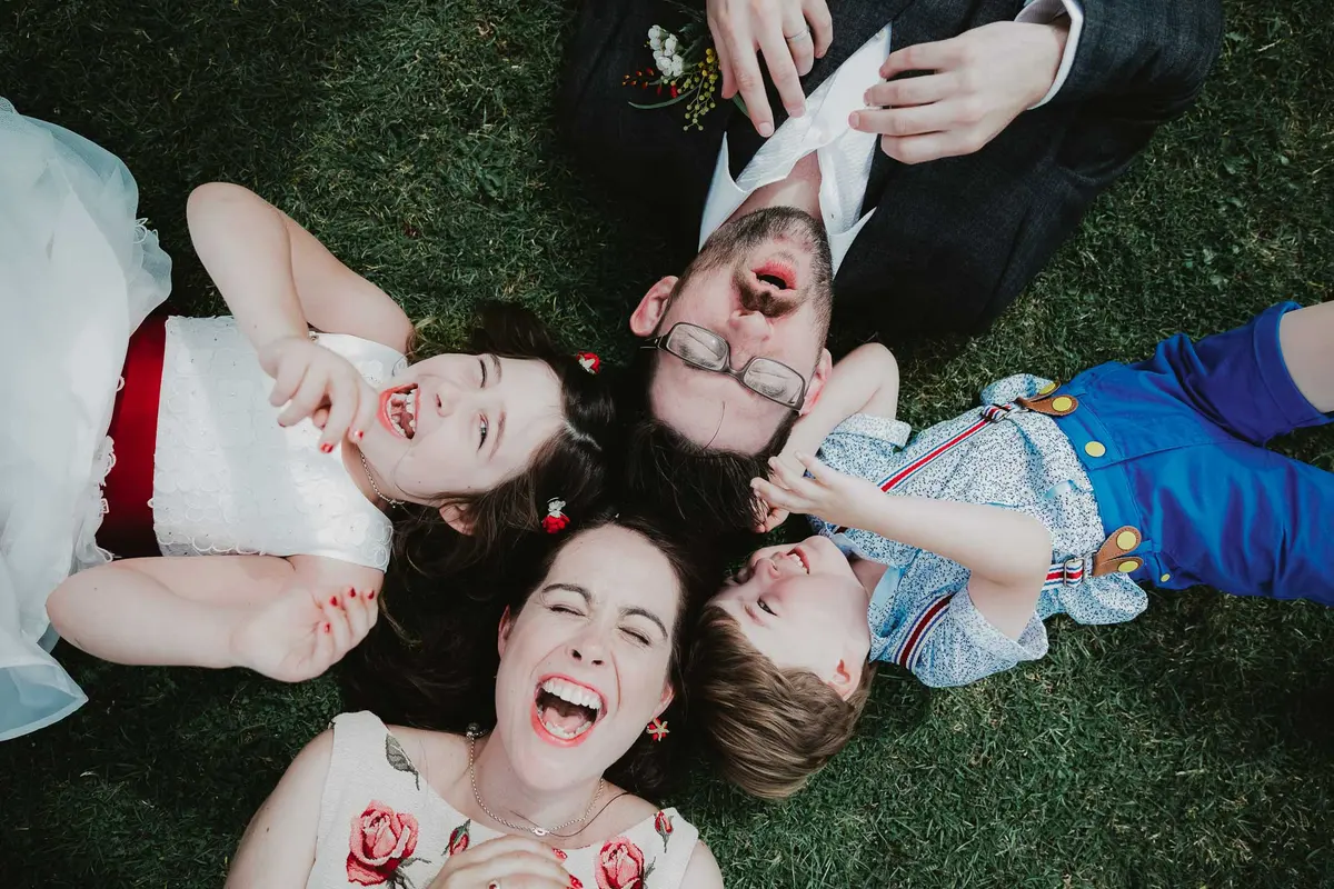 Bride, groom and both their children lying on the grass at their Oxford Wedding