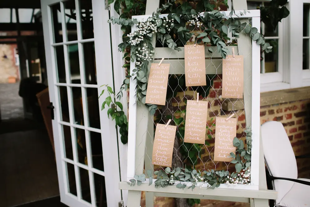 Table plan of handwritten brown tags on a white frame decorated with eucalyptus