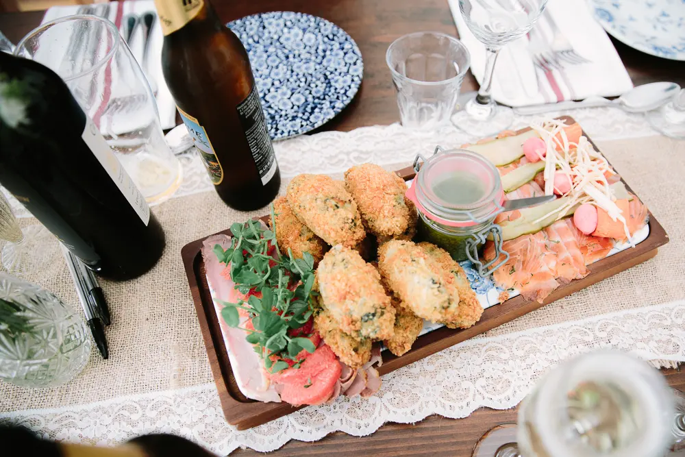 Wooden sharing board of croquettes, ham, smoked salmon and pickles on a lace table runner