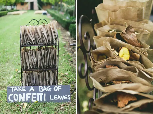 Wire stand of paper bags filled with dried leaves under a chalk sign reading Take a bag of confetti leaves