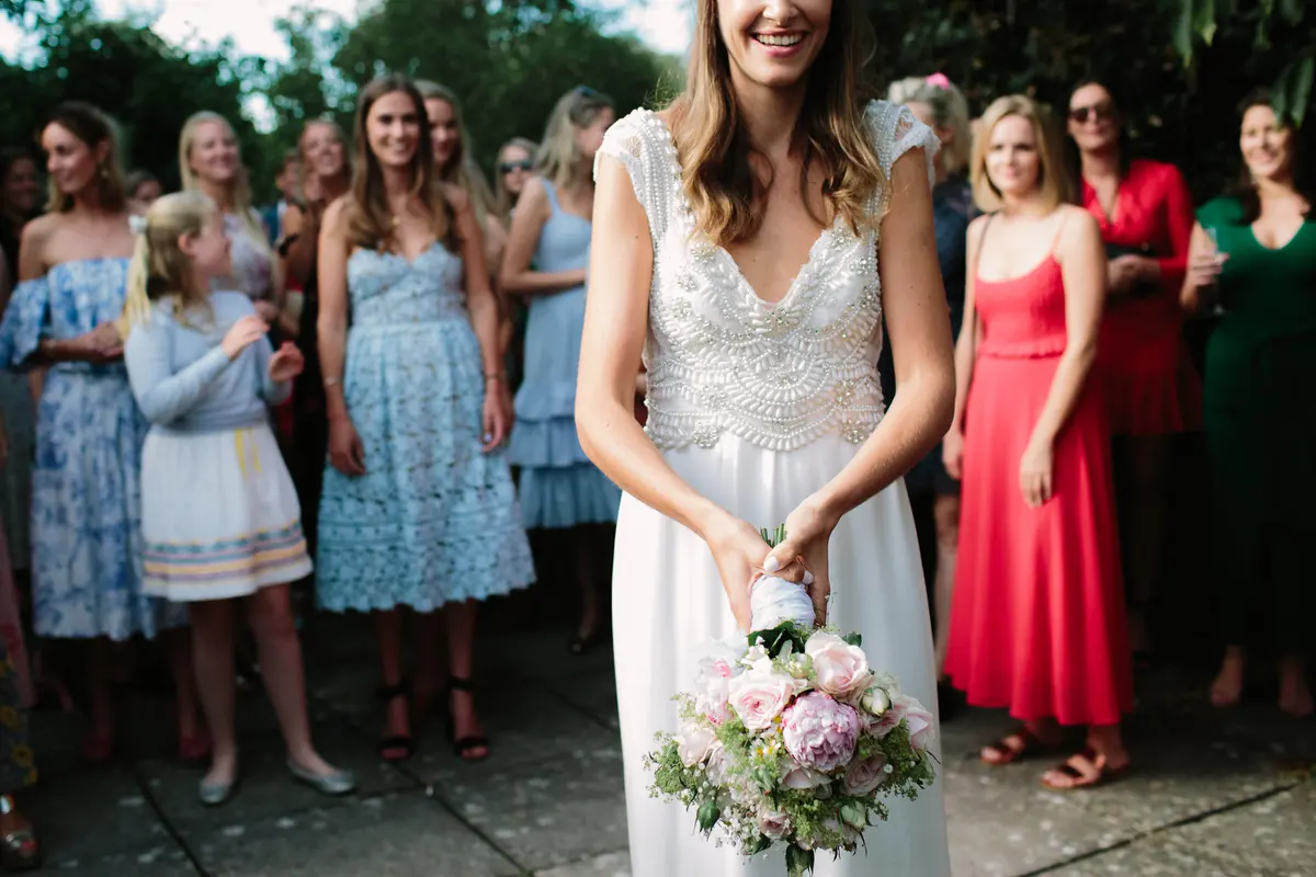 Bride holding her bouquet ready to throw it as female guests wait behind her