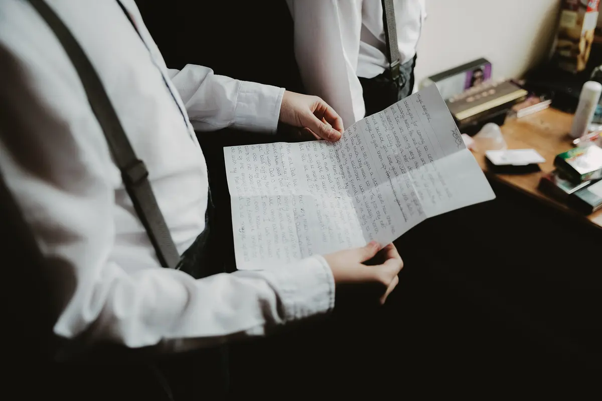 Groomsman in braces reading a handwritten letter while getting ready