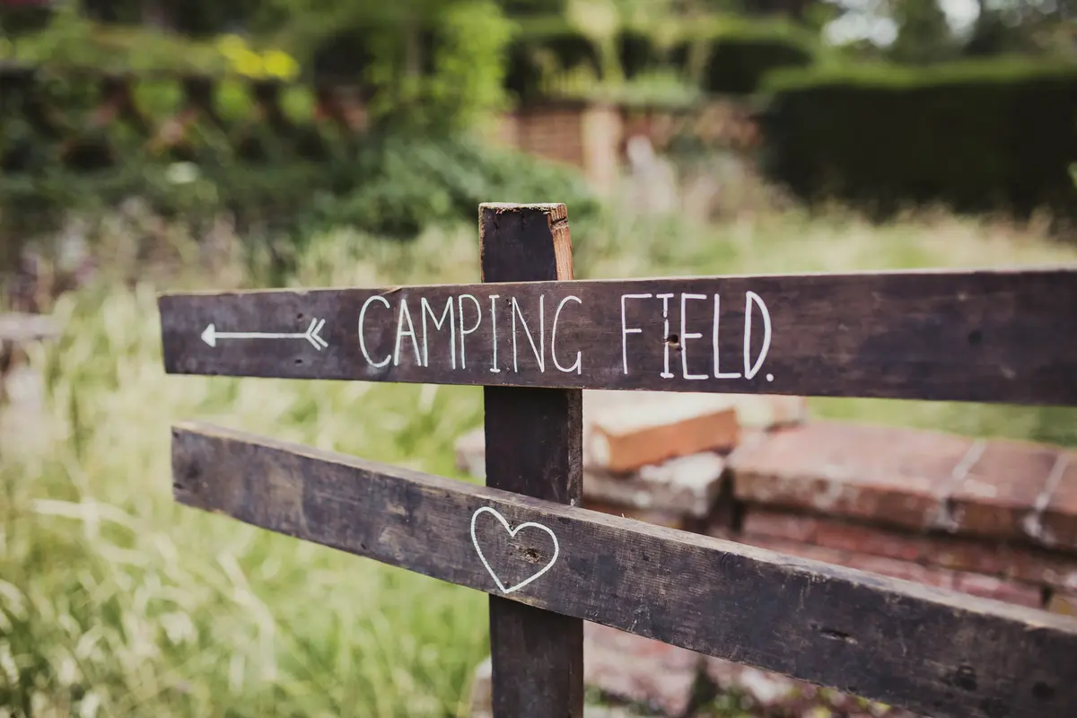 Hand-painted wooden sign with an arrow pointing to the camping field