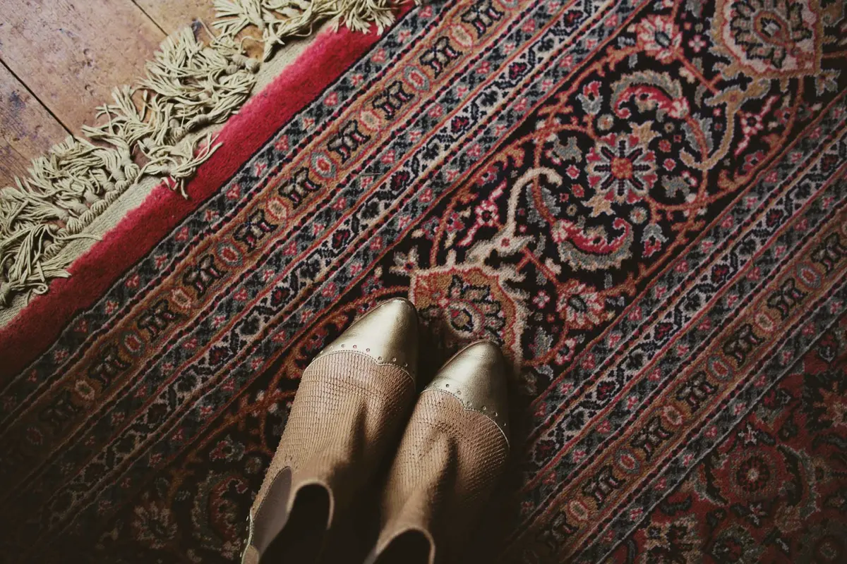 Looking down at the bride's gold-toed ankle boots on a patterned red rug