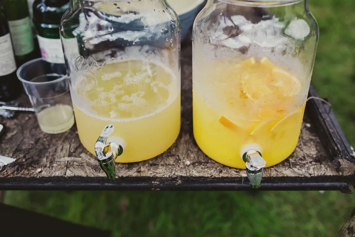 Glass drinks dispensers of lemonade with orange slices on a rustic table outdoors