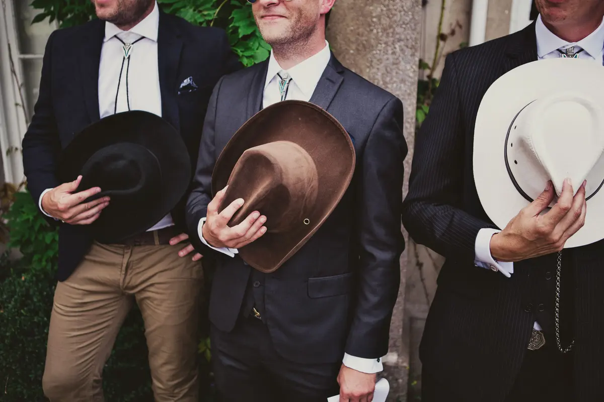 Groomsmen in suits and bolo ties holding their cowboy hats to their chests