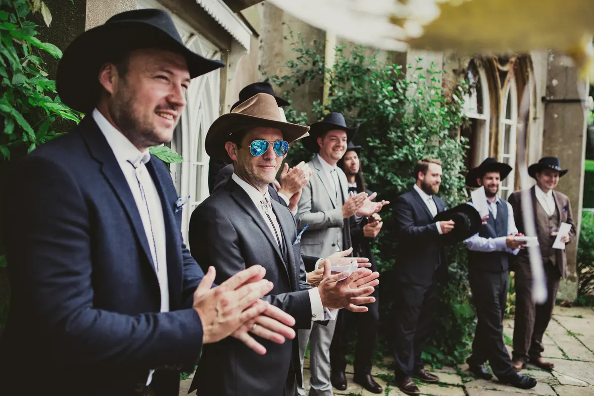 Groomsmen in suits and cowboy hats applauding during the outdoor ceremony