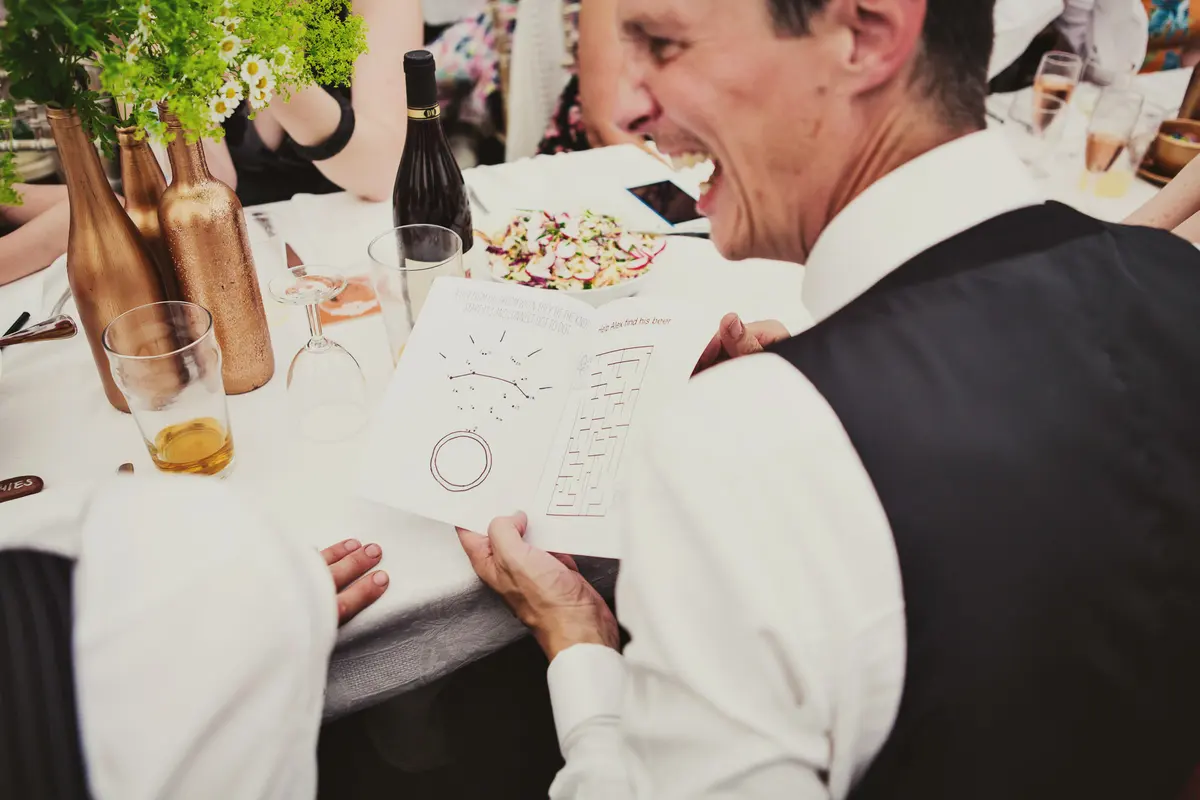 Guest laughing as he holds up an activity sheet at a marquee dinner table