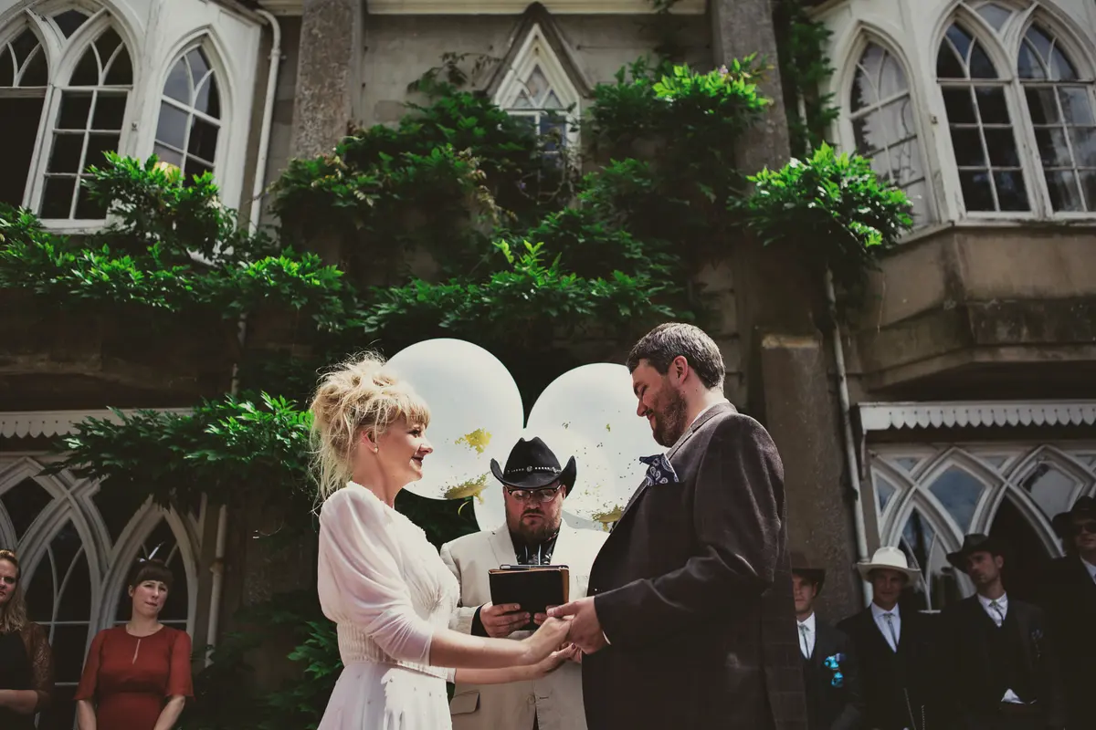 Bride and groom holding hands during their outdoor ceremony led by a celebrant in a cowboy hat