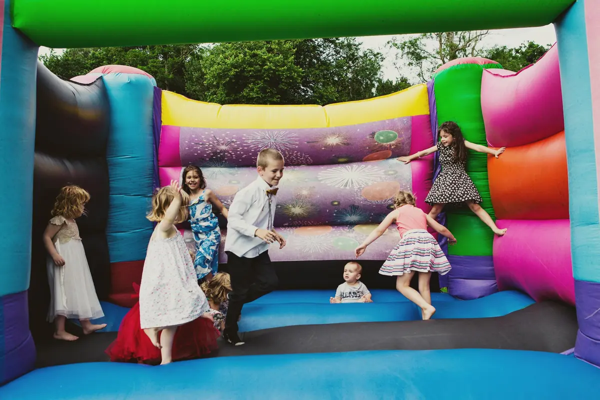 Young wedding guests in party clothes jumping on a bouncy castle