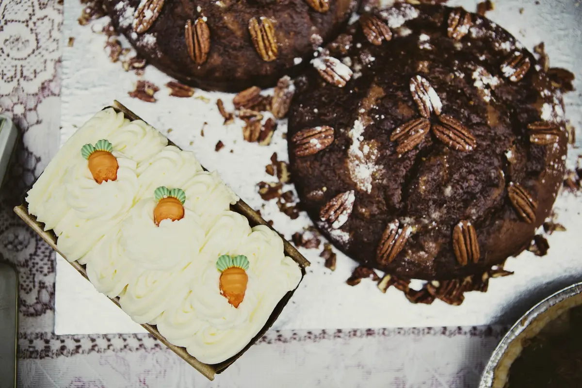 Carrot cake topped with icing carrots beside chocolate pecan cakes on a dessert table