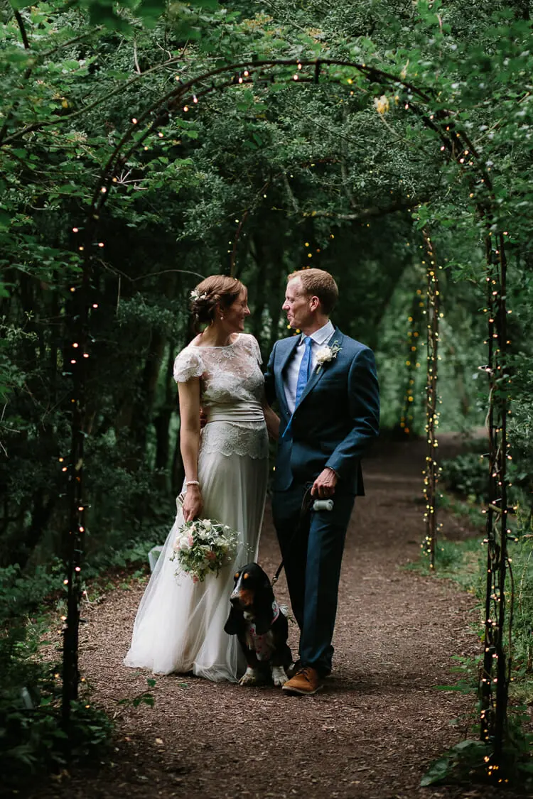 Bride and groom with their dog under the fairy-lit willow arch at the Perch