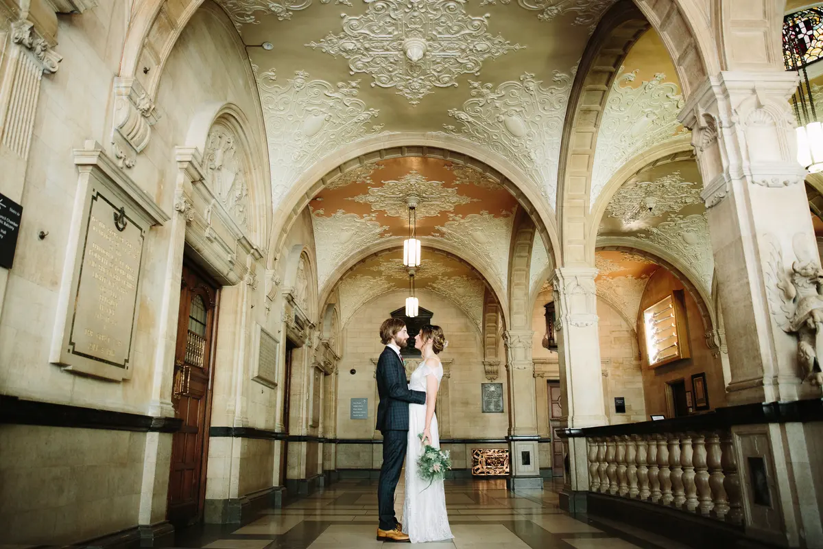 Bride and groom embracing in a grand vaulted hallway with ornate plaster ceilings