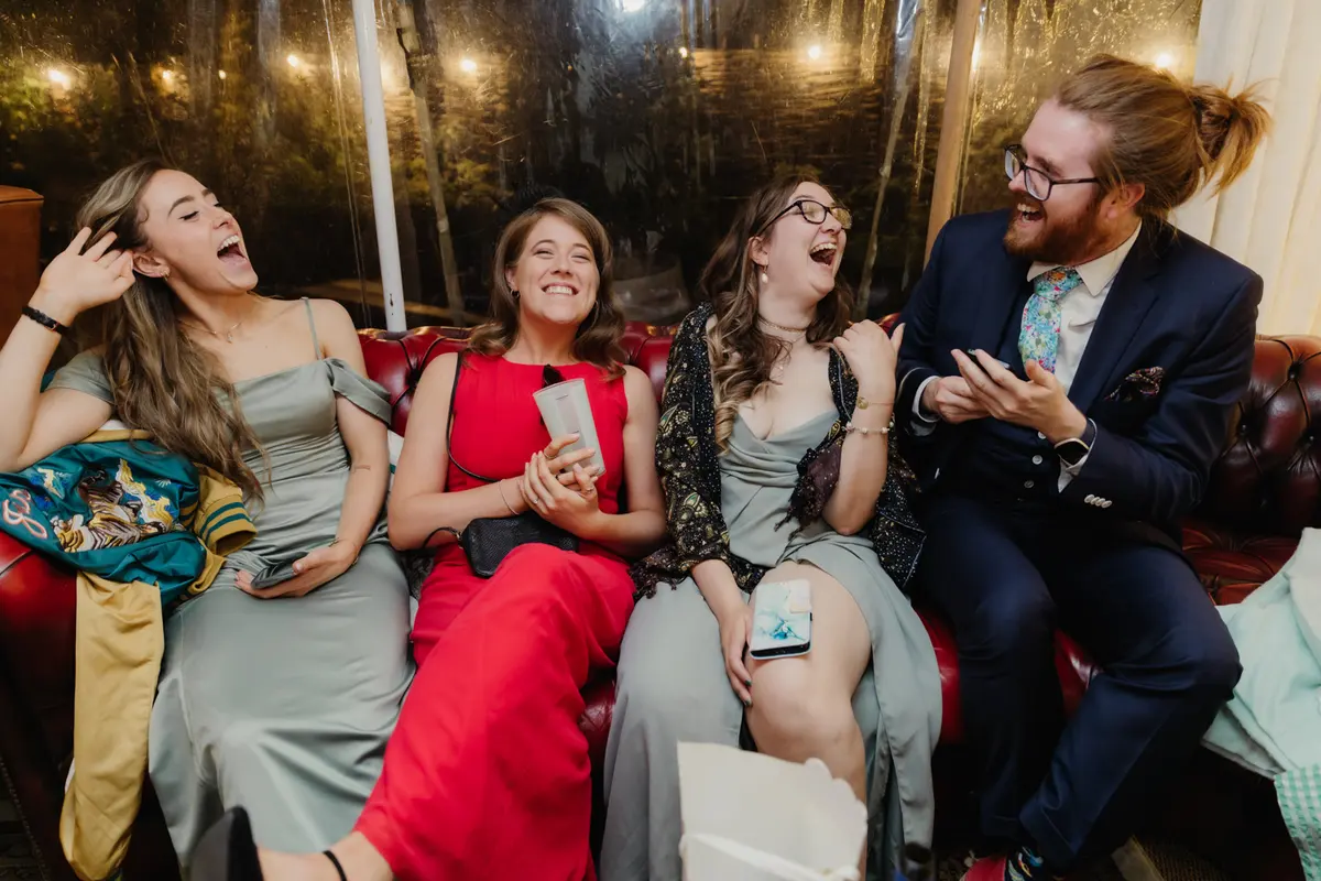 Four guests laughing together on a red leather sofa late in the evening