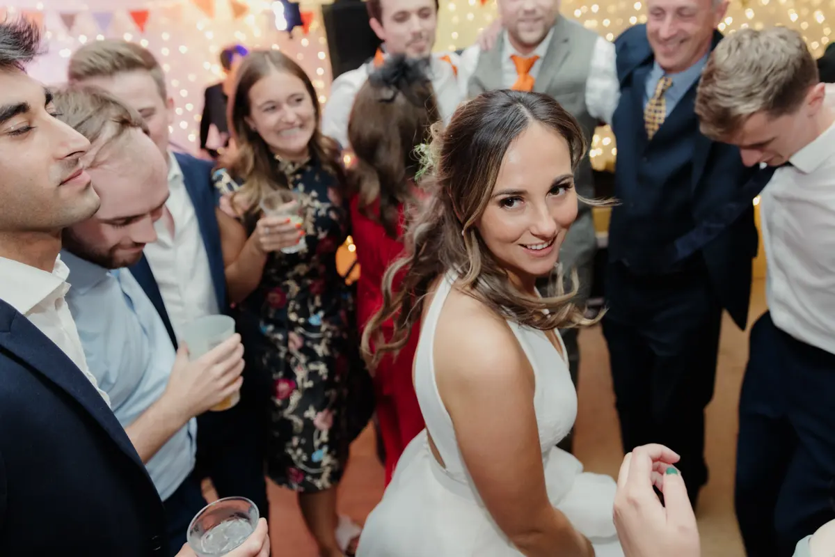 Bride smiling over her shoulder as guests gather round her on the dance floor