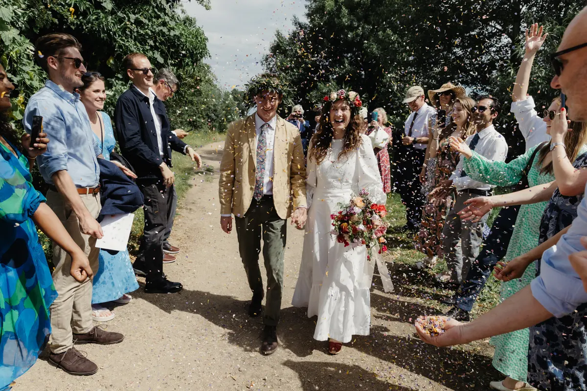 Bride and groom in flower crowns walking hand in hand through falling confetti at the Perch