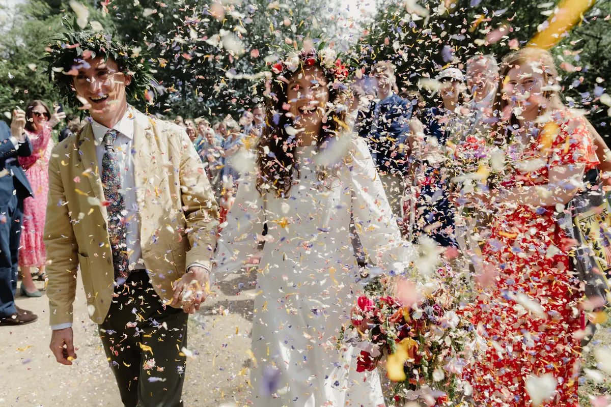Bride and groom laughing in a thick shower of colourful petal confetti