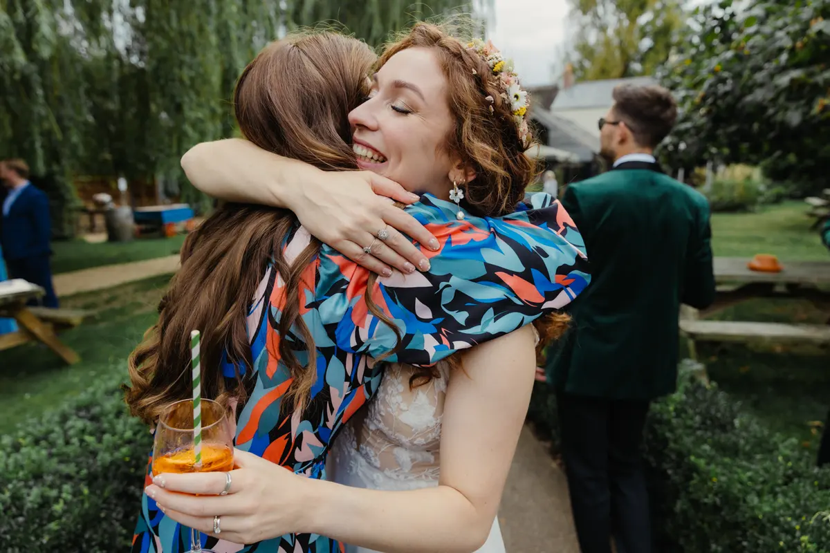 Bride hugging a guest in a colourful scarf in the garden at the Perch