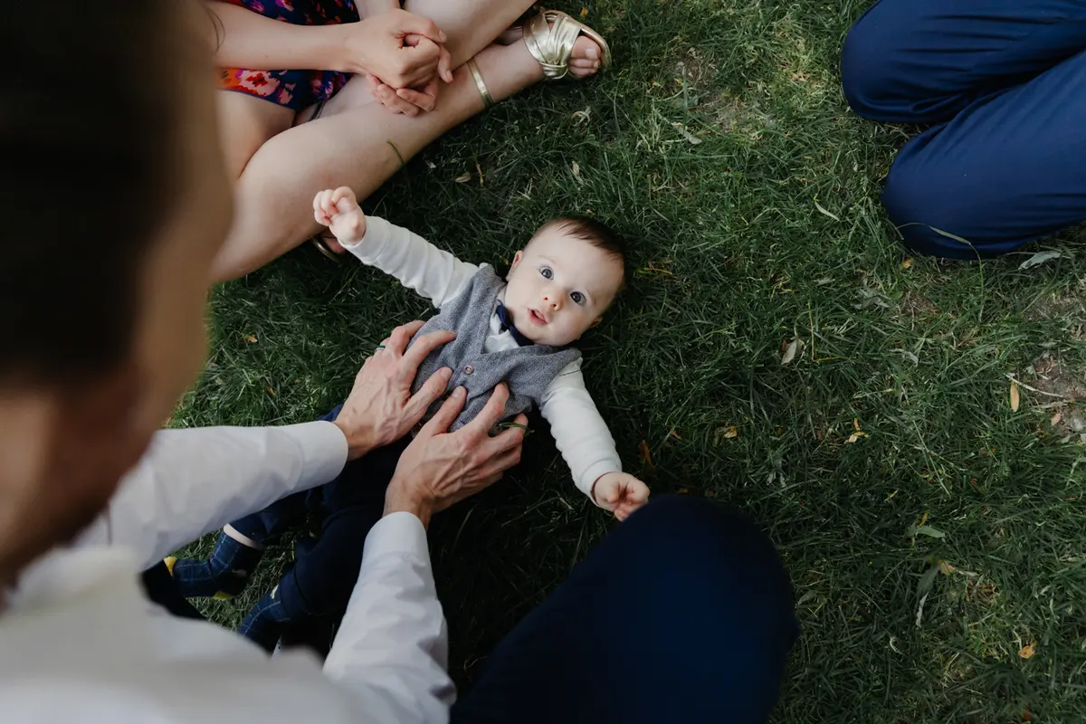 Baby in a waistcoat and bow tie lying on the grass surrounded by family