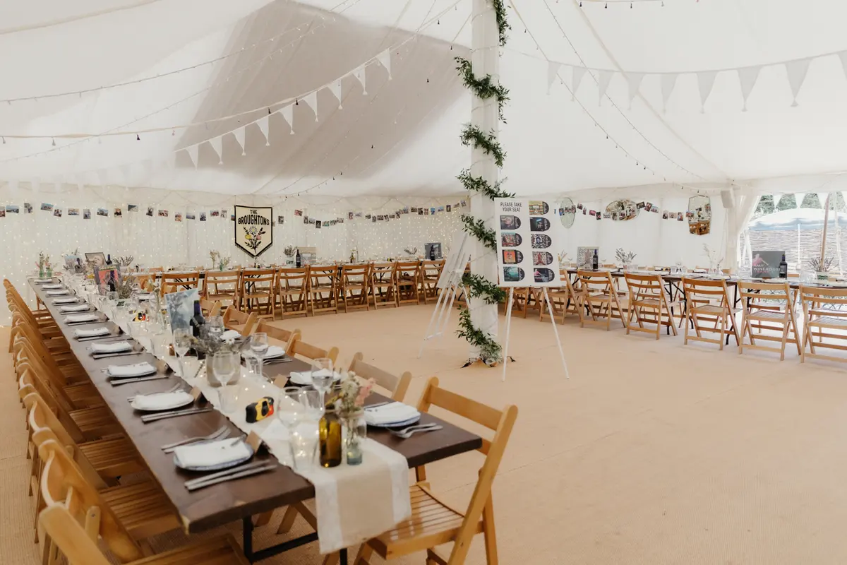 Marquee at the Perch laid with long wooden tables, bunting and fairy lights for the wedding breakfast