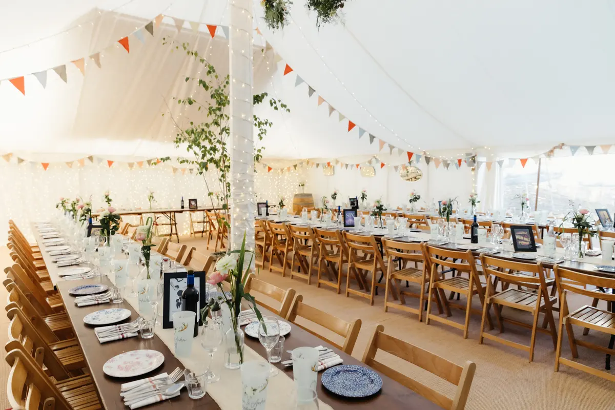 Marquee laid with long wooden tables, folding chairs, bunting and fairy lights at the Perch