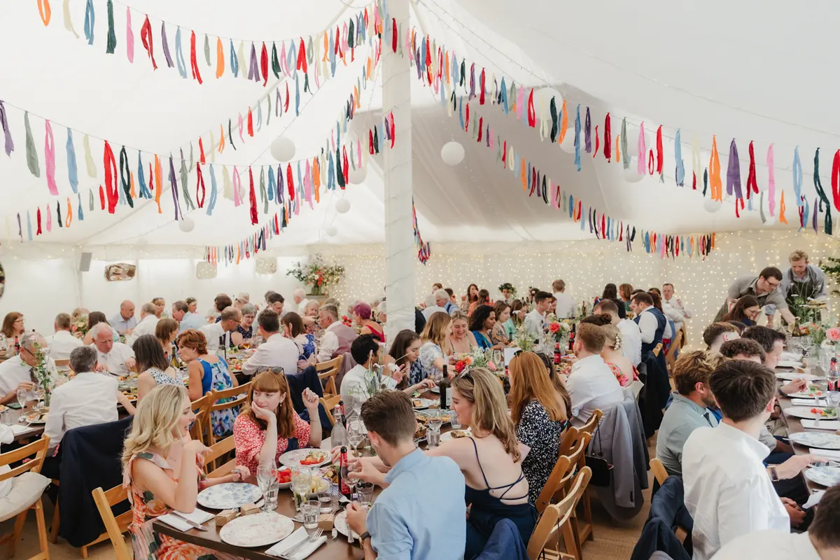 Guests seated at long tables under colourful ribbon bunting in the marquee at the Perch