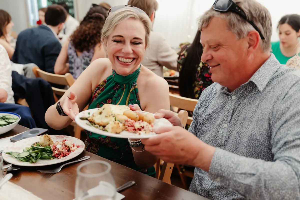 Smiling guest passing a plate of food to a man at the marquee tables