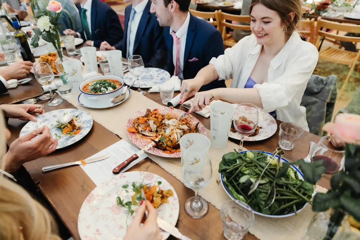Guests passing sharing dishes along a long table during the wedding breakfast
