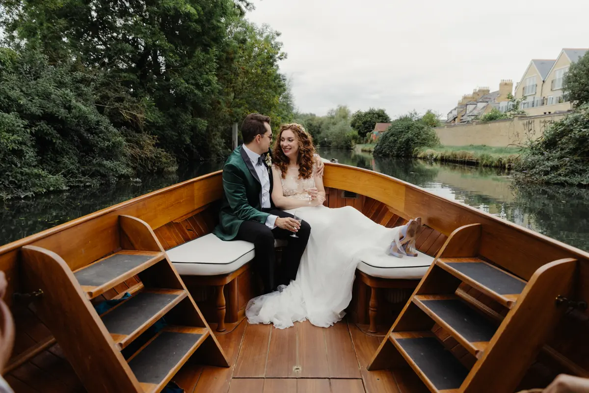 Bride and groom sitting together at the back of a wooden boat on the river
