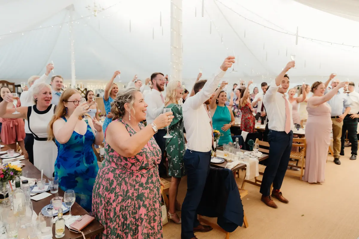 Guests standing at their tables raising glasses for a toast in the marquee