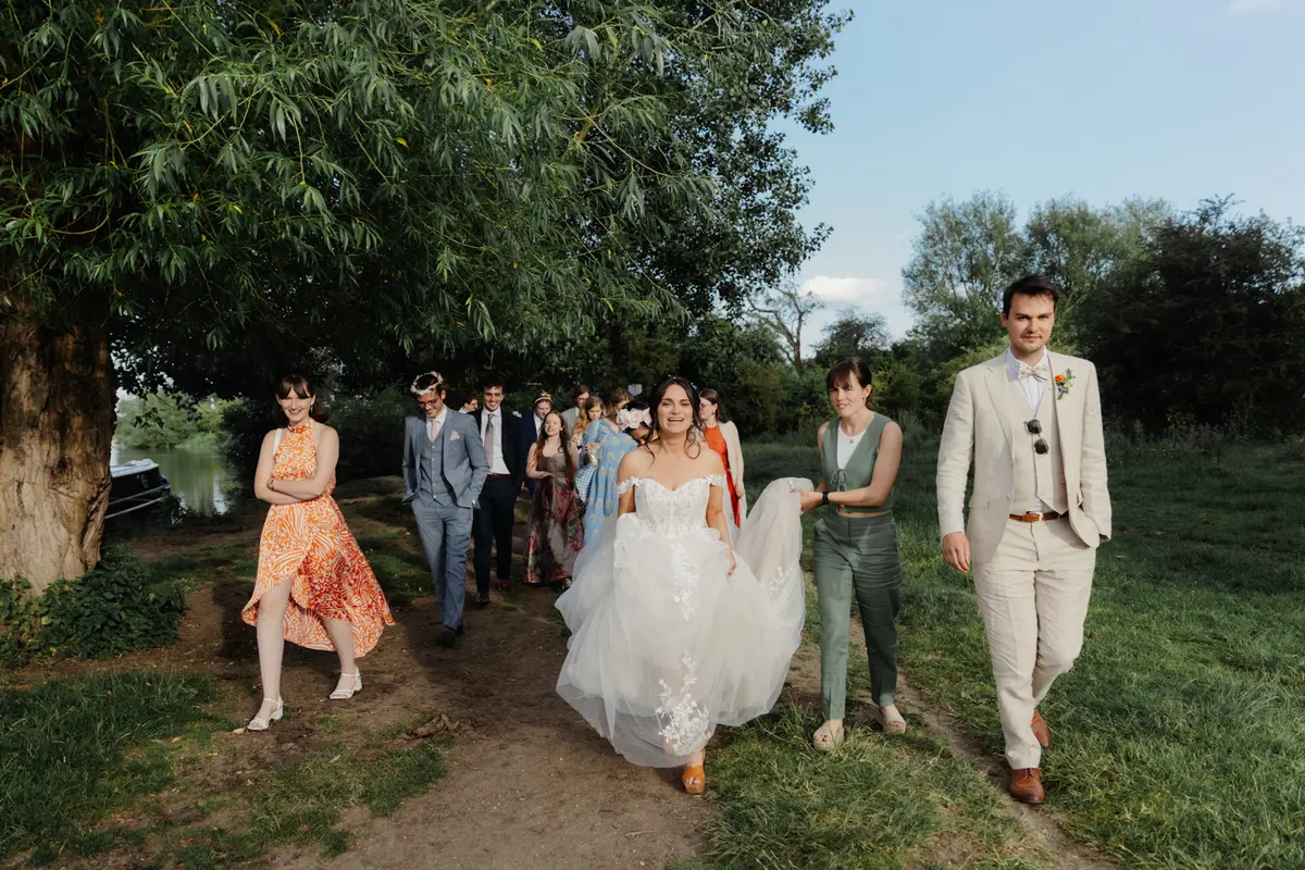 Bride walking along the riverside path at the Perch with the groom and wedding guests