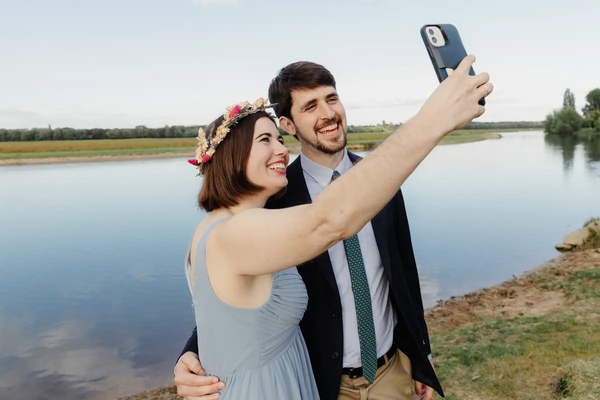 Guest in a flower crown taking a selfie with her partner beside Port Meadow