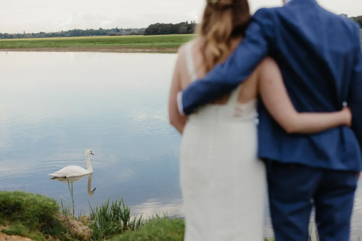 Couple with their arms around each other watching a swan on the water at Port Meadow