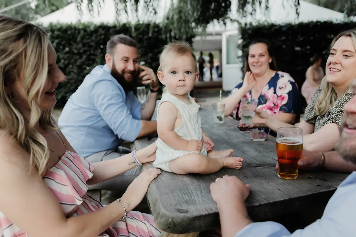Baby sitting on a pub garden table surrounded by smiling guests at the Perch