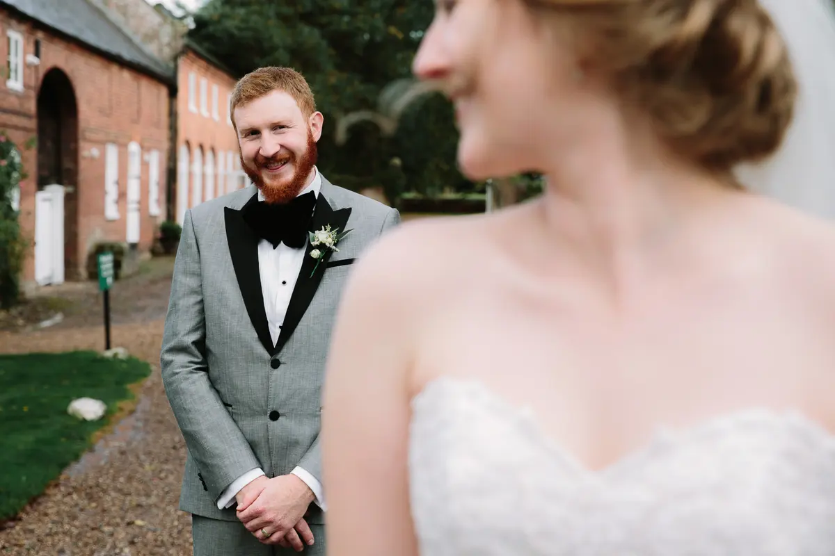 Groom in a grey tuxedo smiling as he sees the bride for the first time