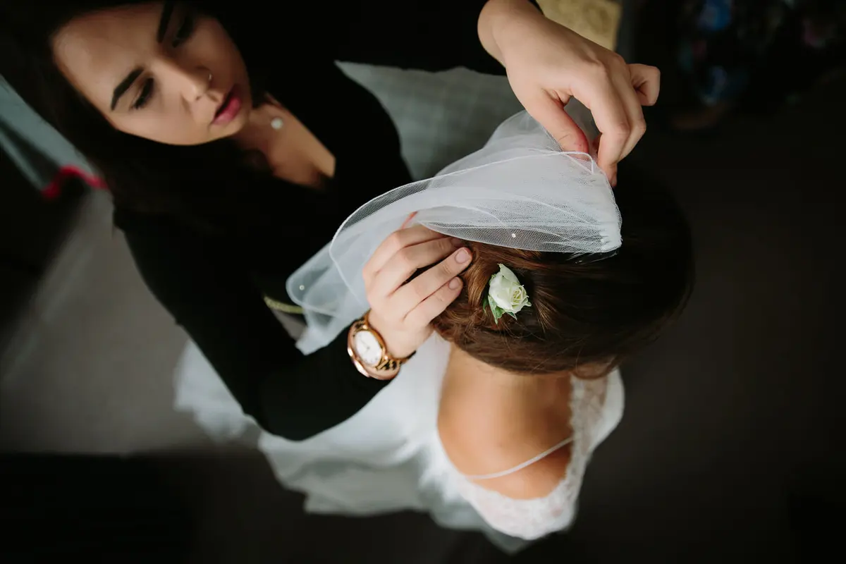 Bride having her veil fixed into her hair beside a white rose, seen from above
