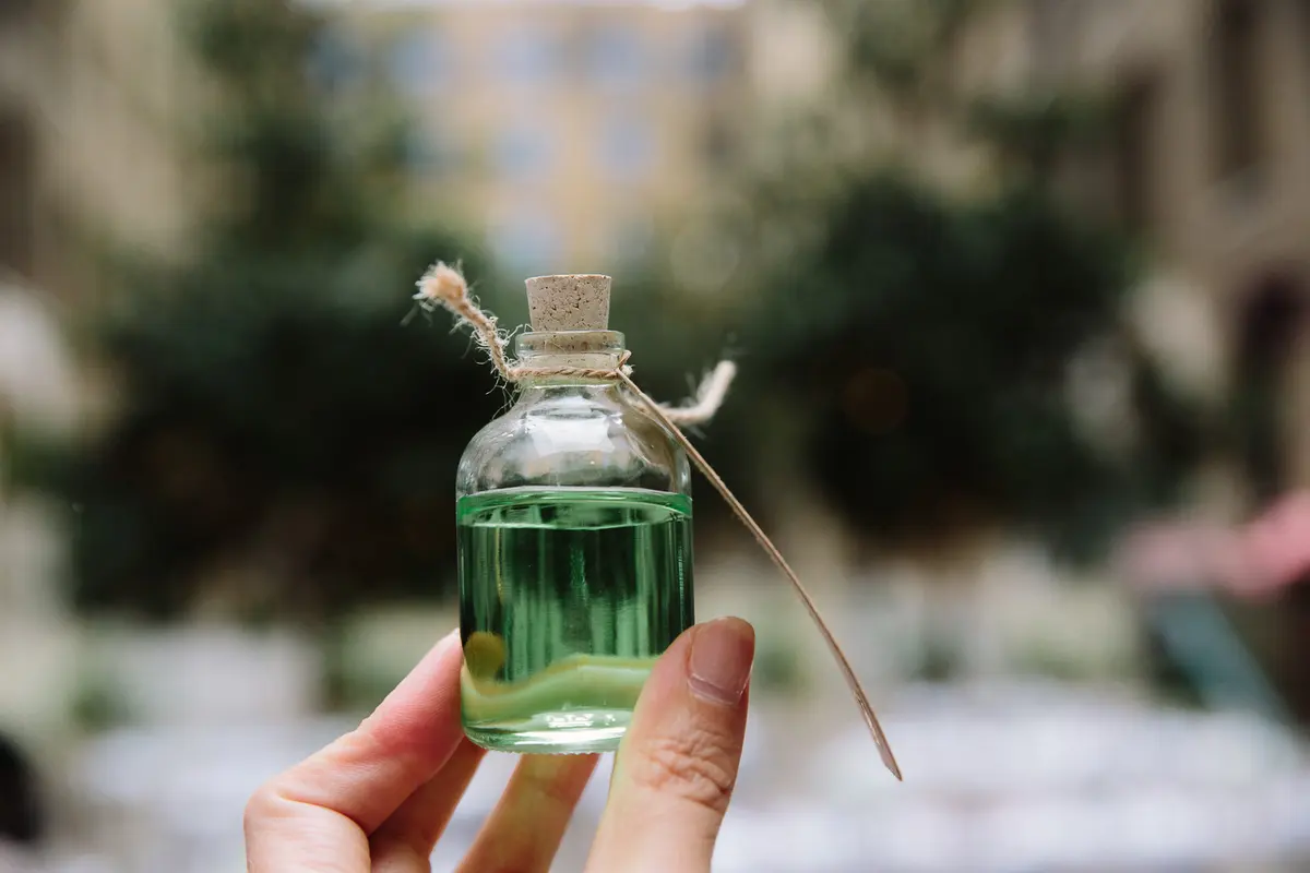 Hand holding a small corked glass bottle of green liquid in a courtyard