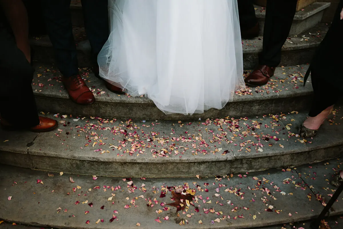 Bride's tulle skirt and guests' shoes on stone steps scattered with petal confetti