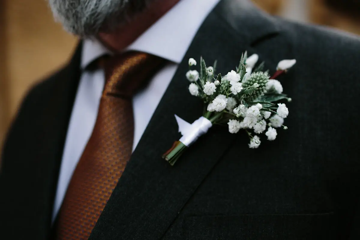 Close-up of a gypsophila and thistle buttonhole on a dark suit with a copper tie