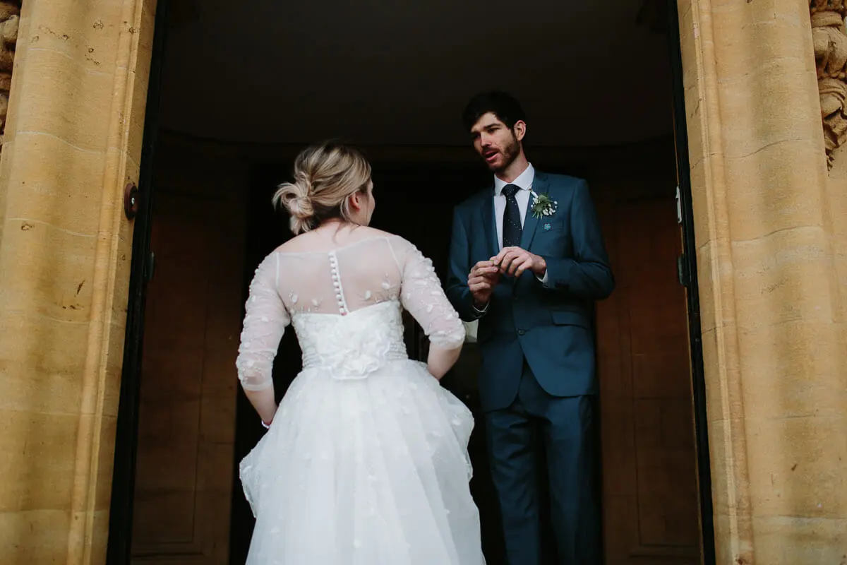 Groom talking to the bride as she reaches him in a tall stone doorway