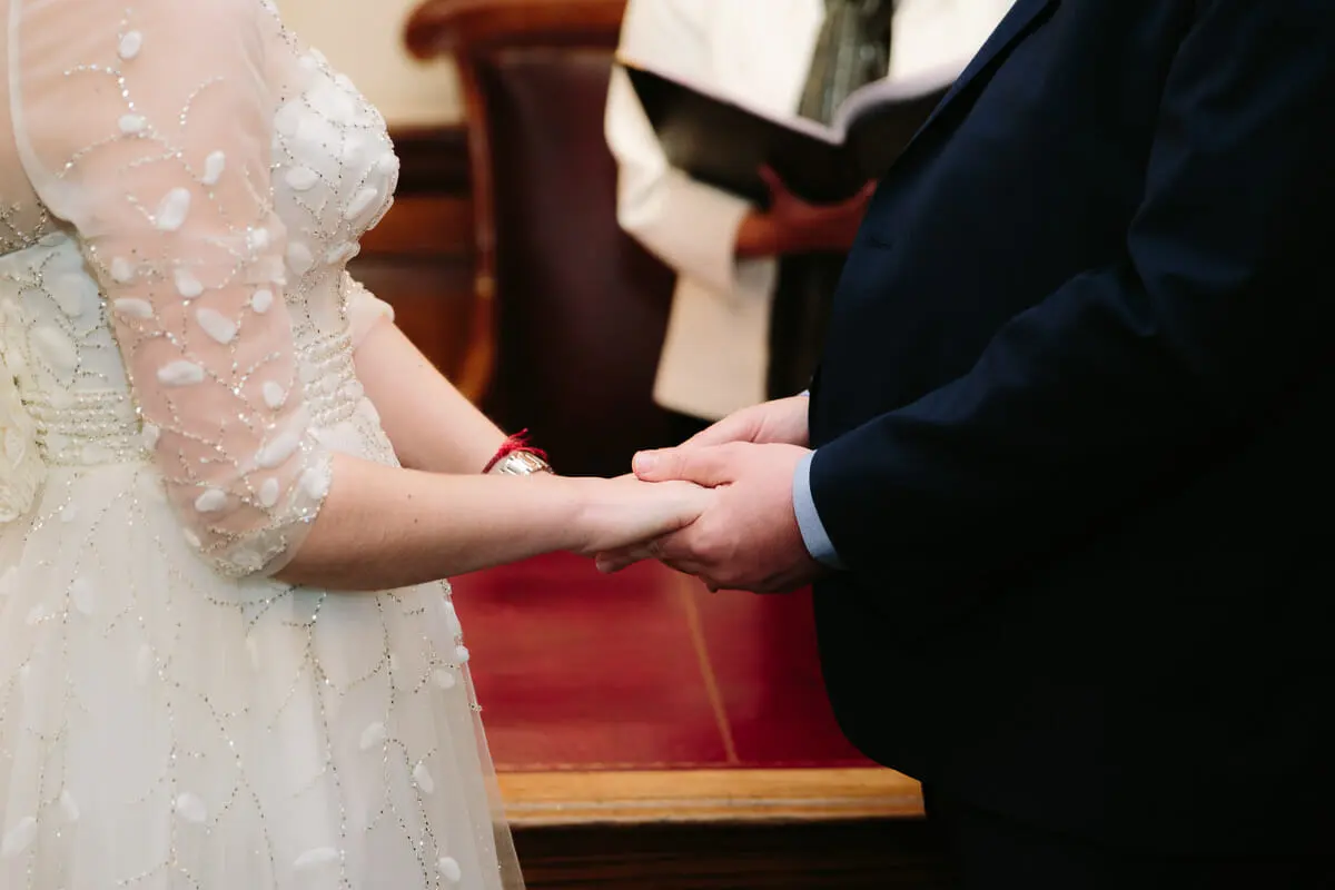 Close-up of the bride and groom holding hands as the registrar reads