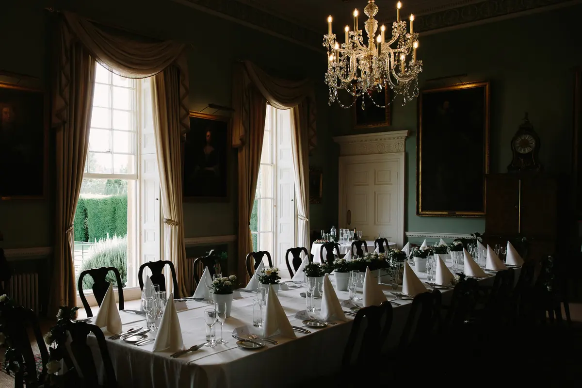 Long dining table laid for a small wedding under a chandelier in a room with tall windows