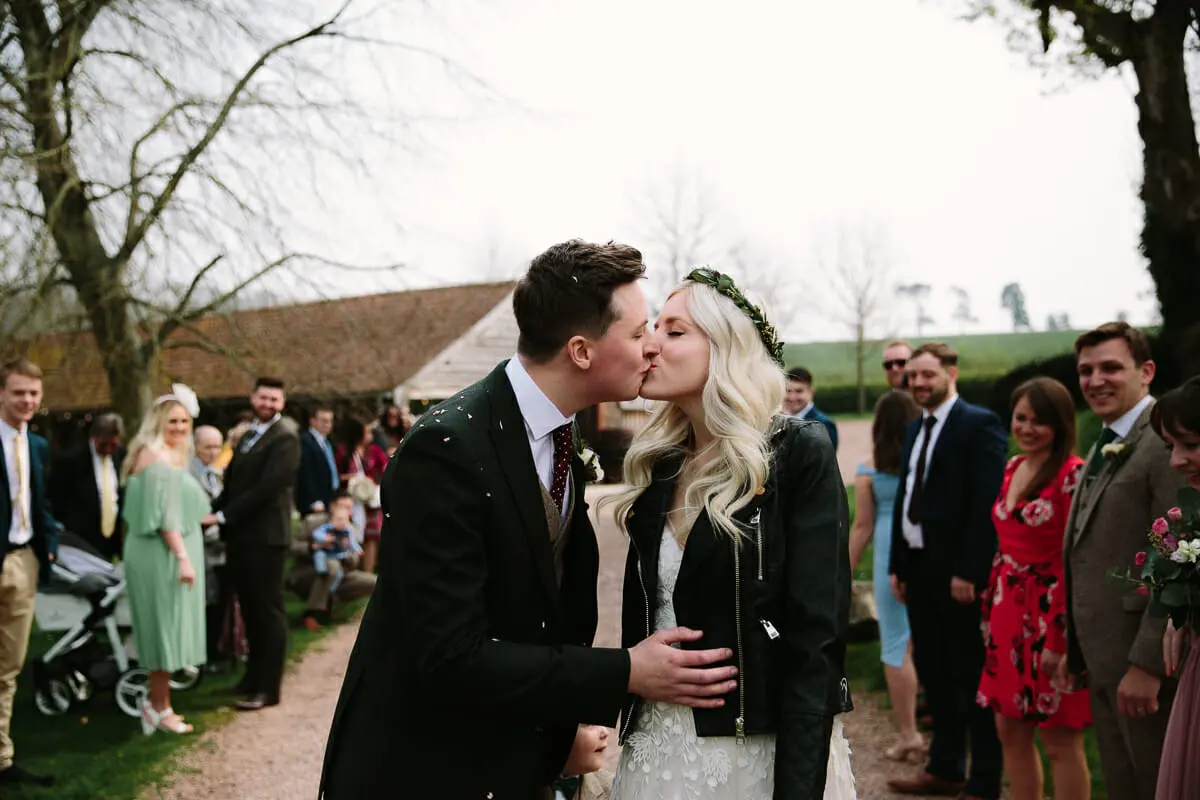 Bride and groom kissing on a gravel path lined with guests after the confetti throw