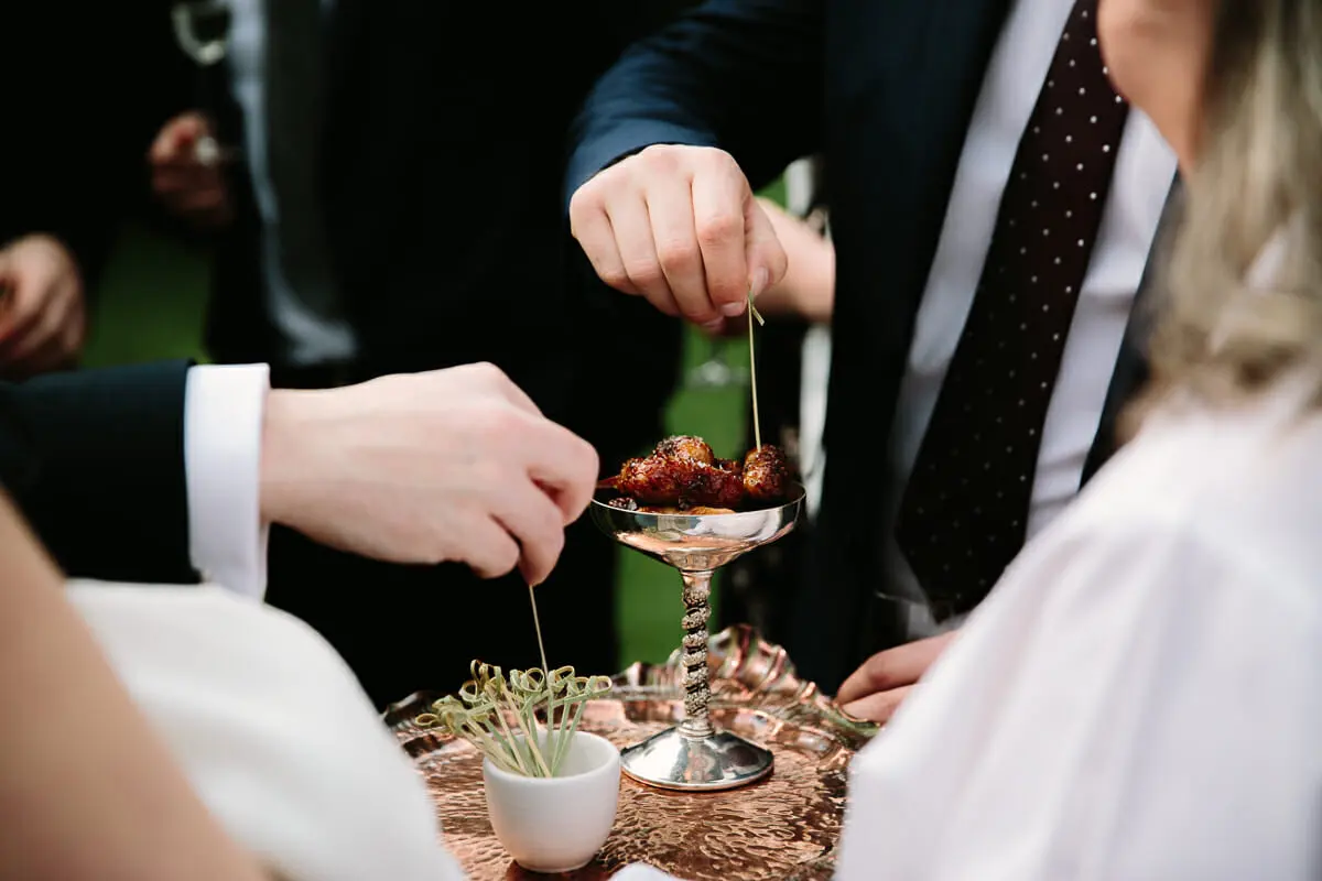 Guests picking canapés on cocktail sticks from a silver bowl on a copper tray
