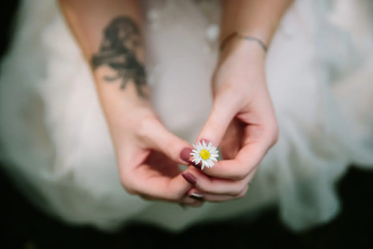 Close view of the bride's hands holding a small daisy against her wedding dress