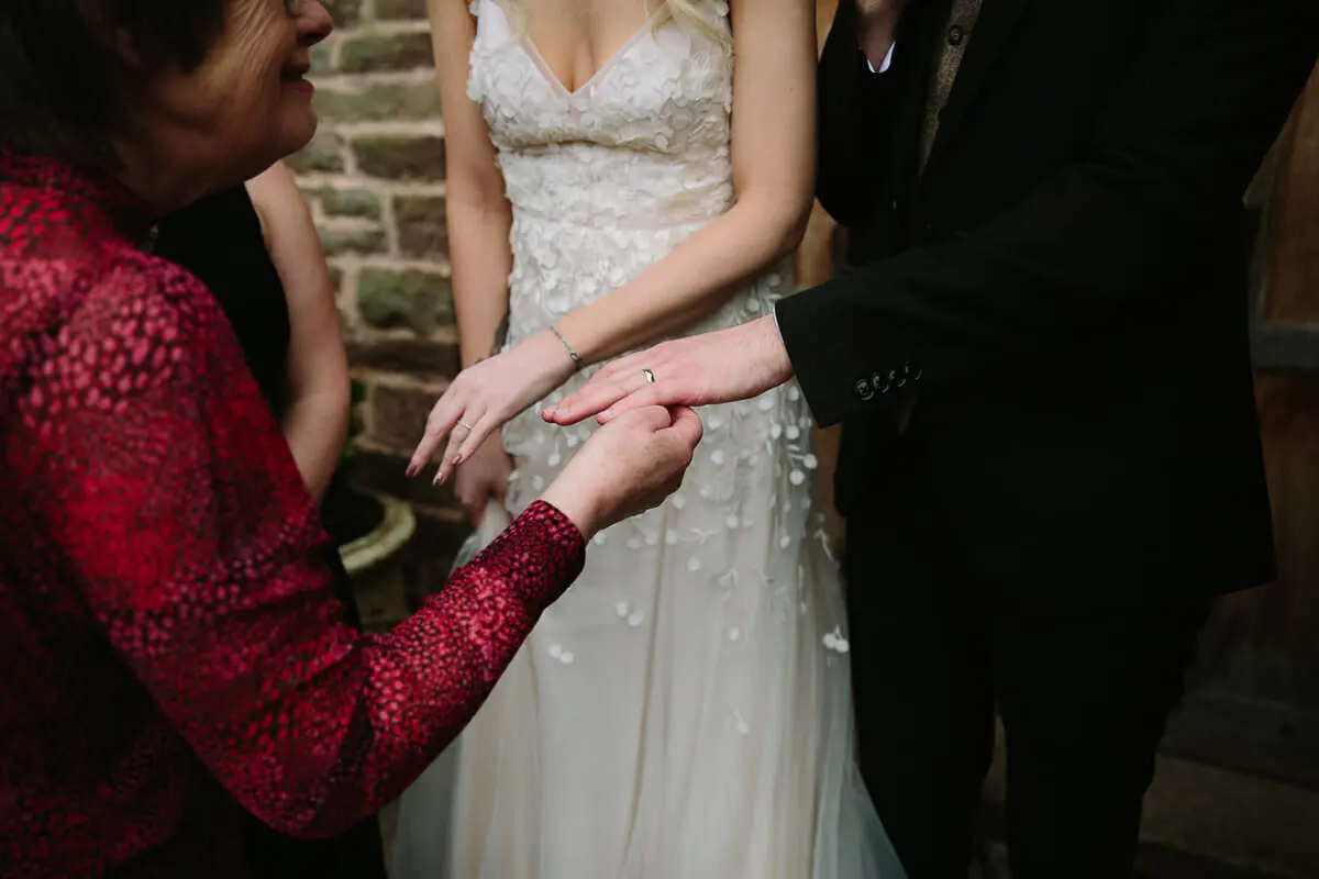 Guest in red lace holding the bride's hand to look at her new wedding ring as the groom shows his