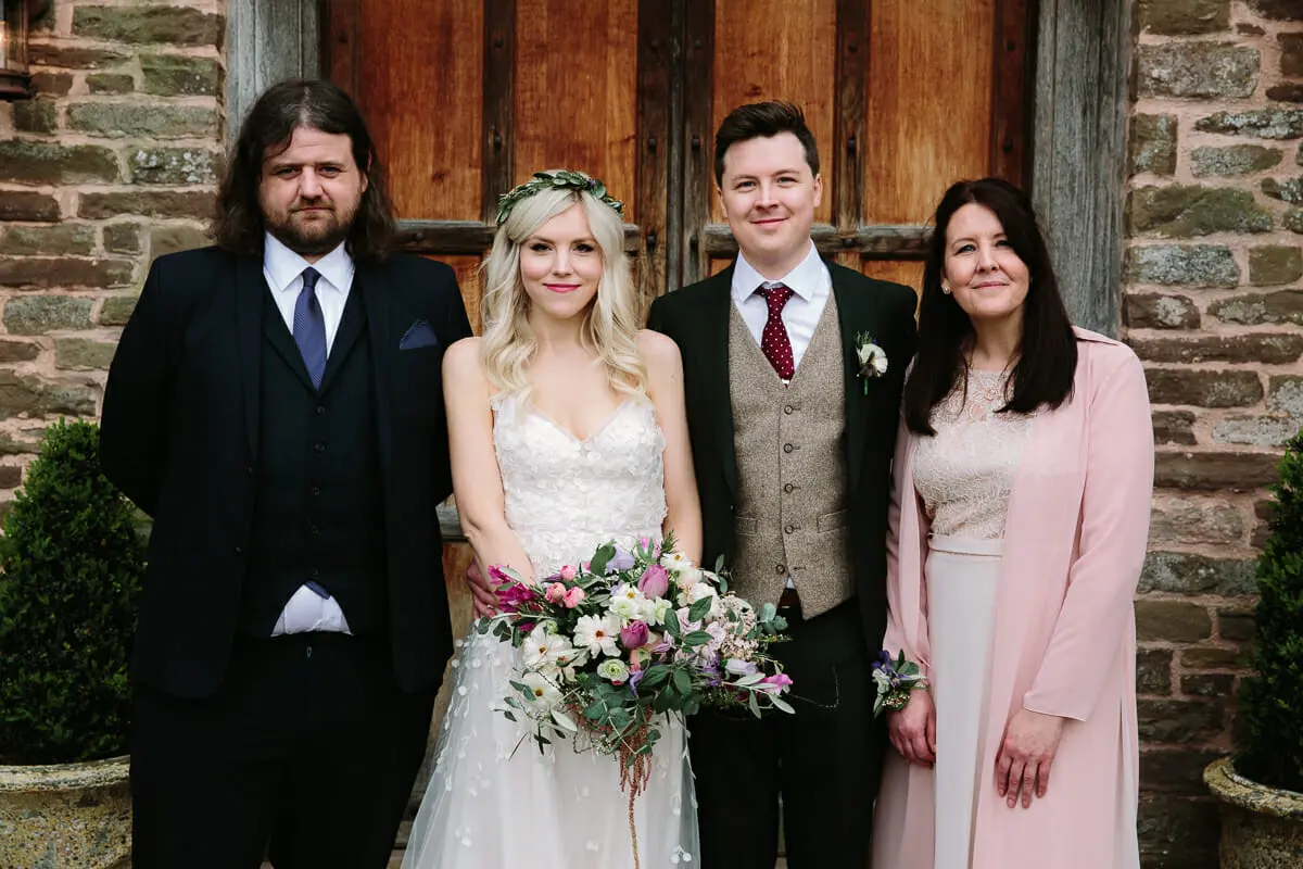Bride and groom with three family members in front of old wooden doors and a stone wall