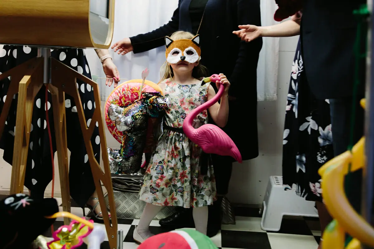 Young girl in a fox mask holding a pink flamingo prop at a wedding photo booth