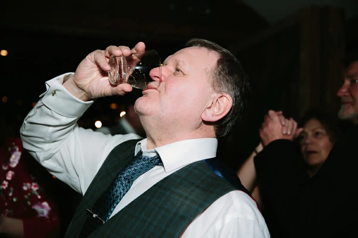 Wedding guest in a checked waistcoat downing a drink at the evening party